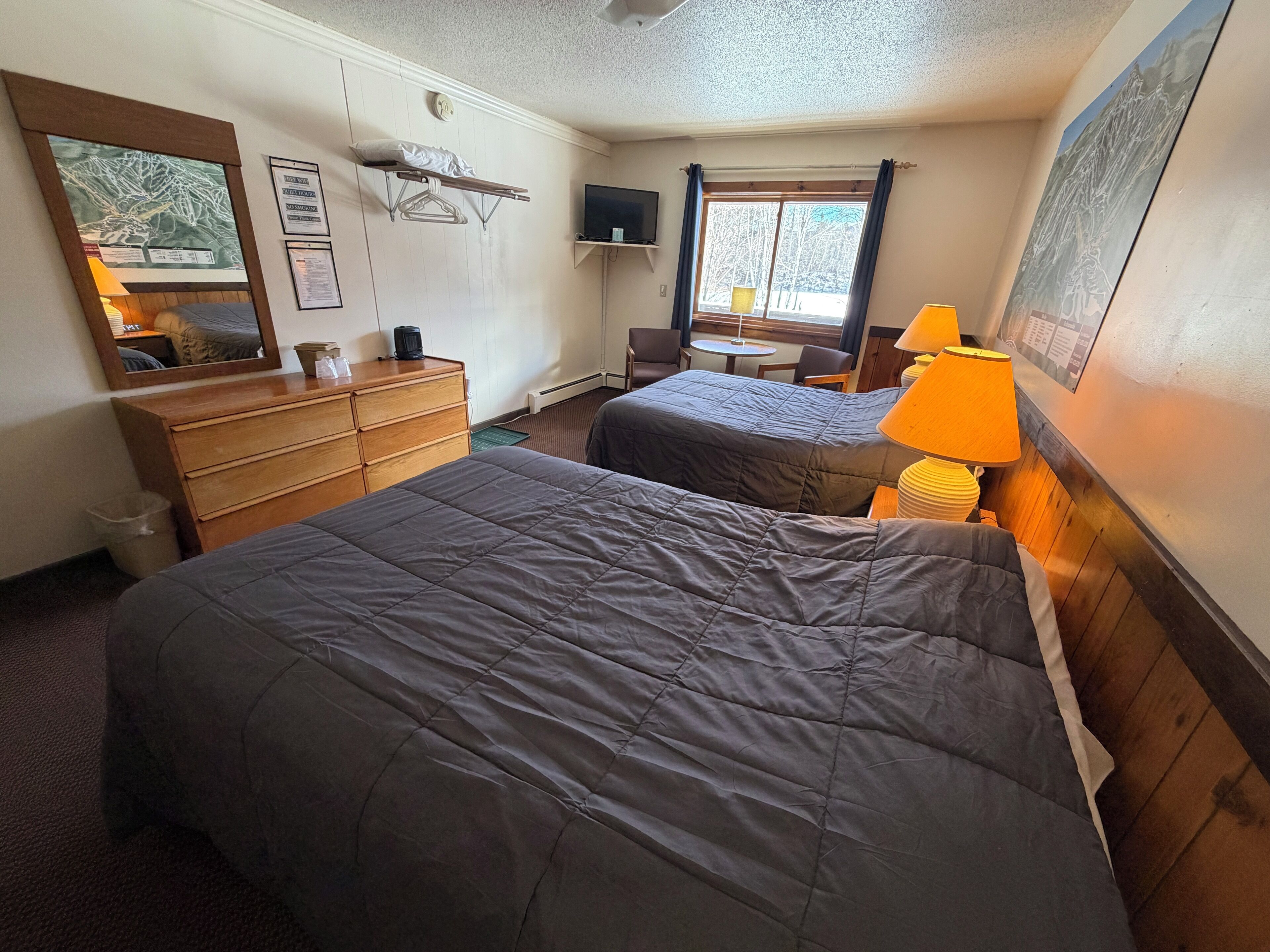 A hotel room with two beds, a dresser, a mirror, a television, and a window with curtains.