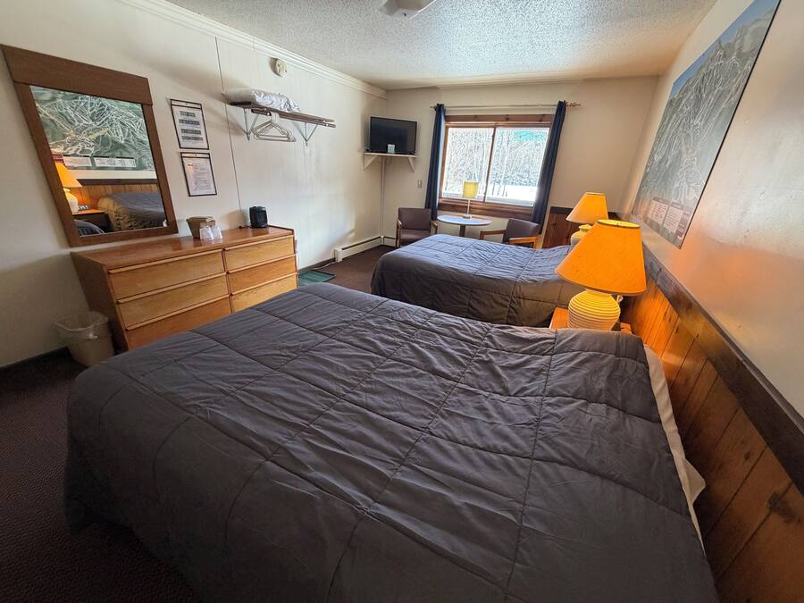 A hotel room with two beds, a dresser, a mirror, a television, and a window with curtains.