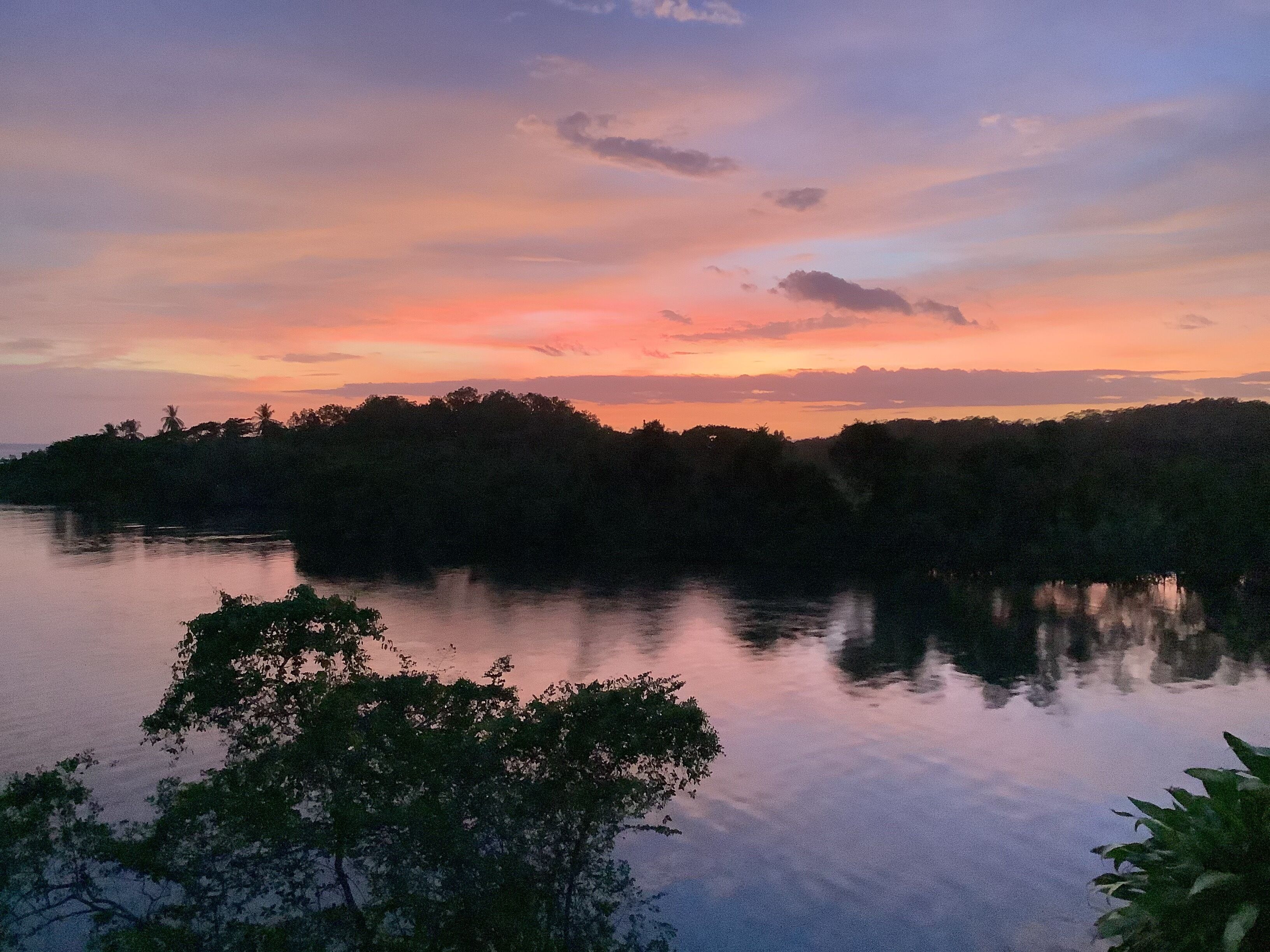A calm lake at sunset with trees reflecting the sky.