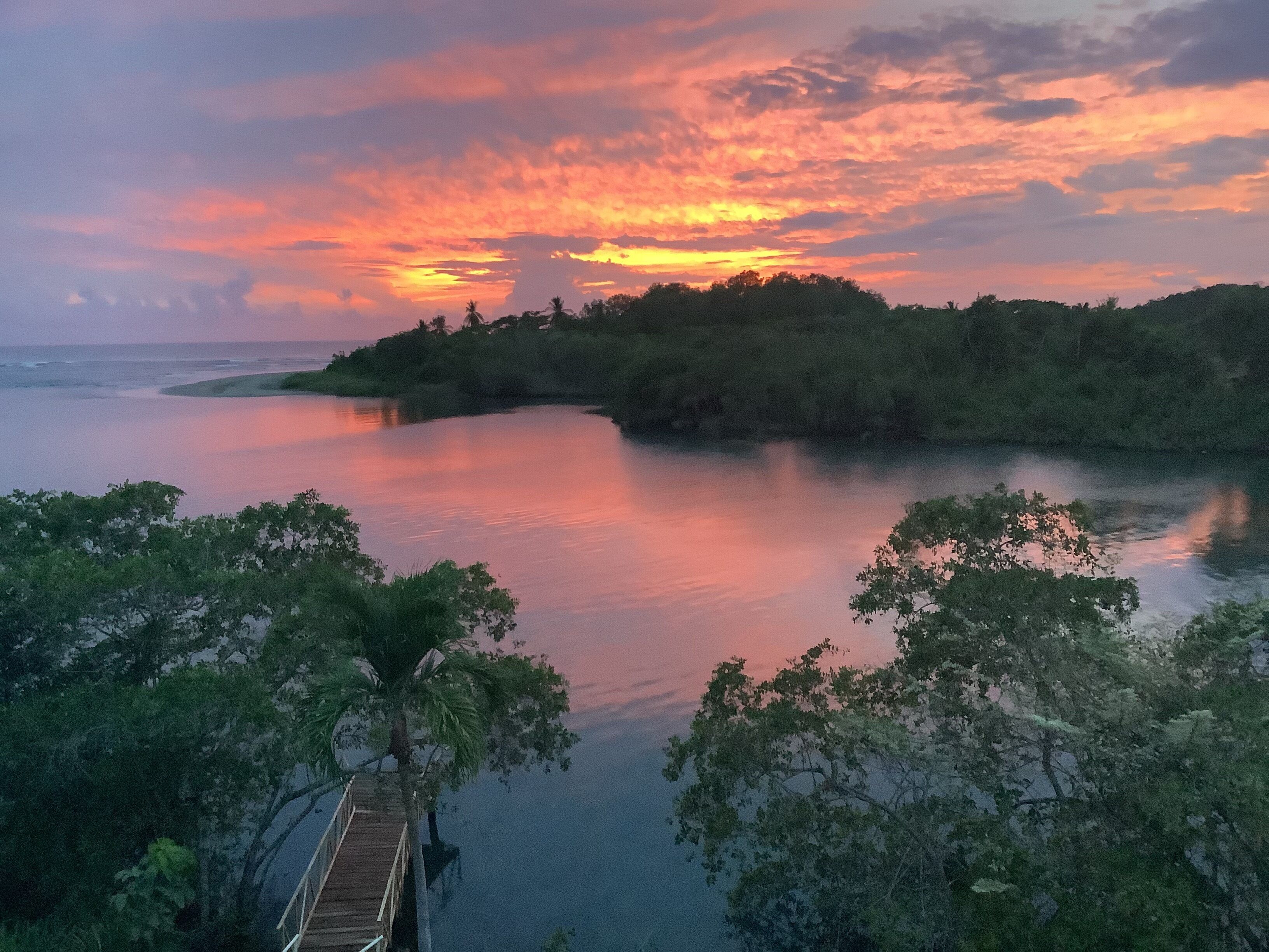 A calm river with a wooden bridge in the foreground and a forested island in the background.