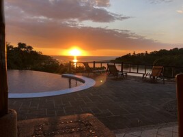 Una piscina curva con vistas al atardecer, sillas de descanso y una terraza de madera.