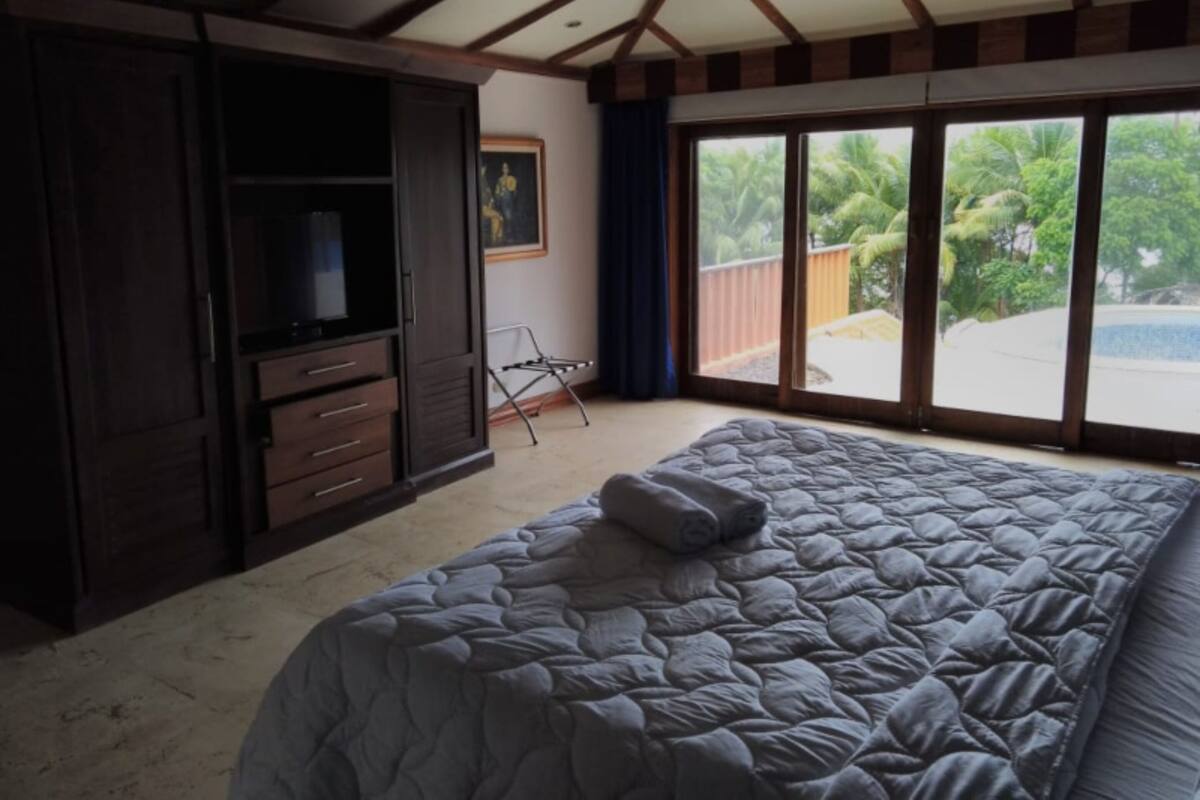 Un dormitorio con una cama grande, un armario, un televisor y vista a una playa desde la ventana.