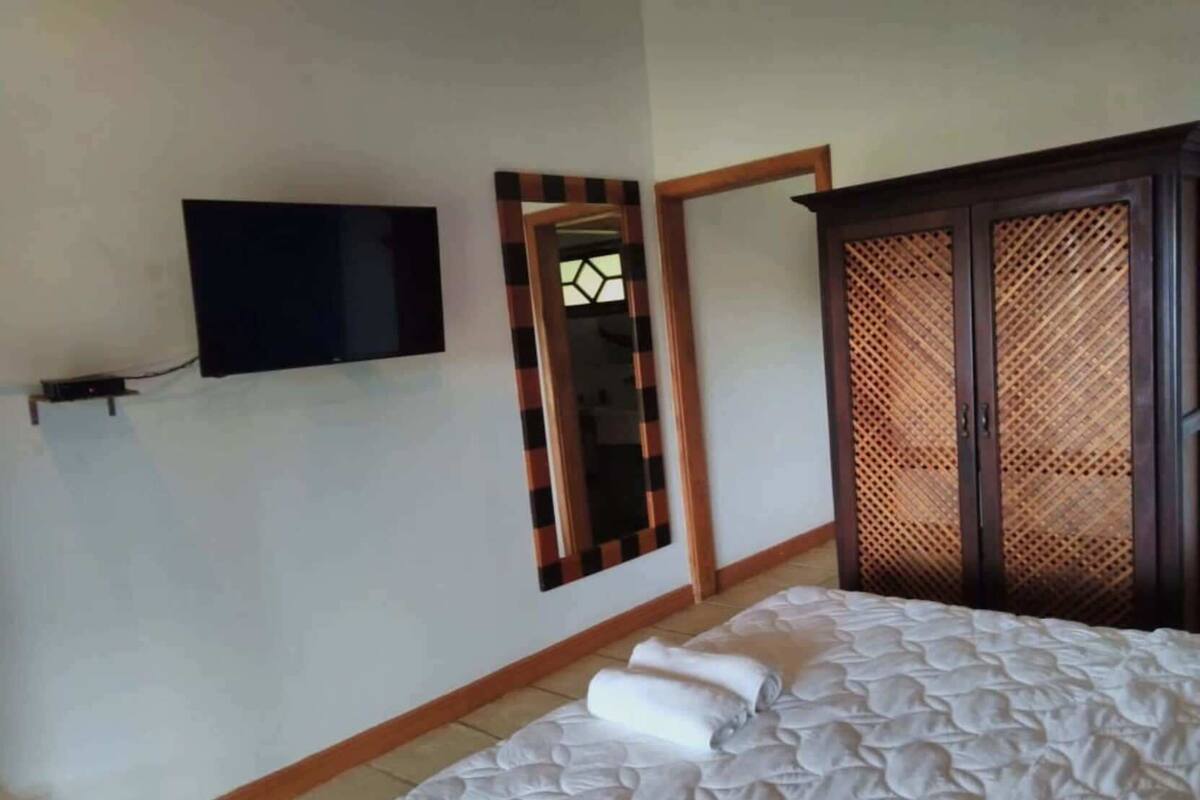 Un dormitorio con una cama, un televisor montado en la pared, un espejo y un armario con diseño de celosía.
