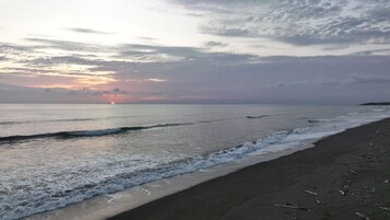 Una playa con olas mansas lamiendo la orilla, un atardecer a lo lejos y un cielo despejado.