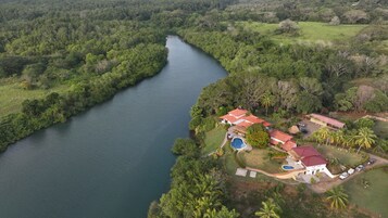 Vista aérea de un complejo turístico con un río, varias edificaciones de techo rojo y una piscina.