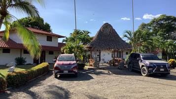 A hotel with a thatched-roof structure, a red car, and a black SUV parked in front.