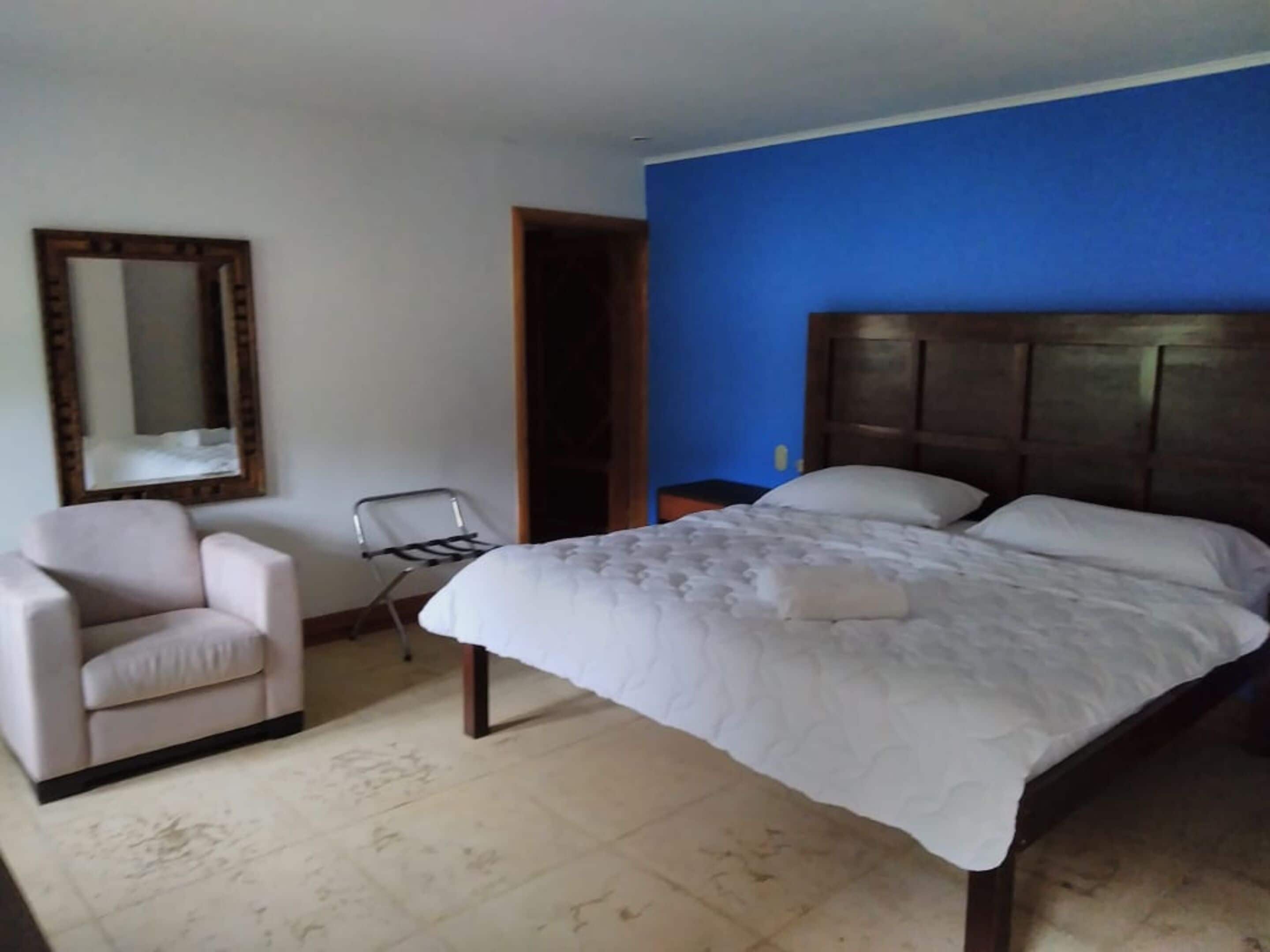 Un dormitorio con cama, una silla, una mesita de noche y un espejo.