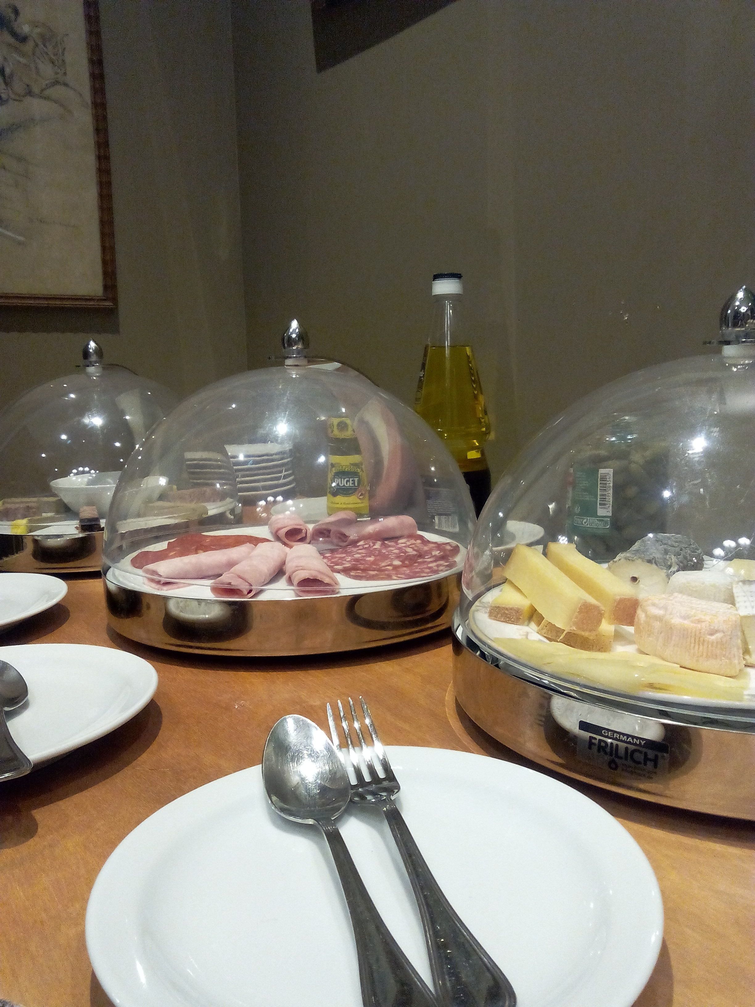 A buffet table with covered food displays, including meats and cheeses, and a bottle of oil.