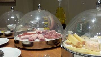 Una mesa de buffet con exhibiciones de comida cubiertas, incluyendo carnes y quesos, y una botella de aceite.