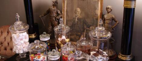 A display of glass jars filled with various candies and chocolates, arranged on a table with a framed picture and two candle-like objects in the background.
