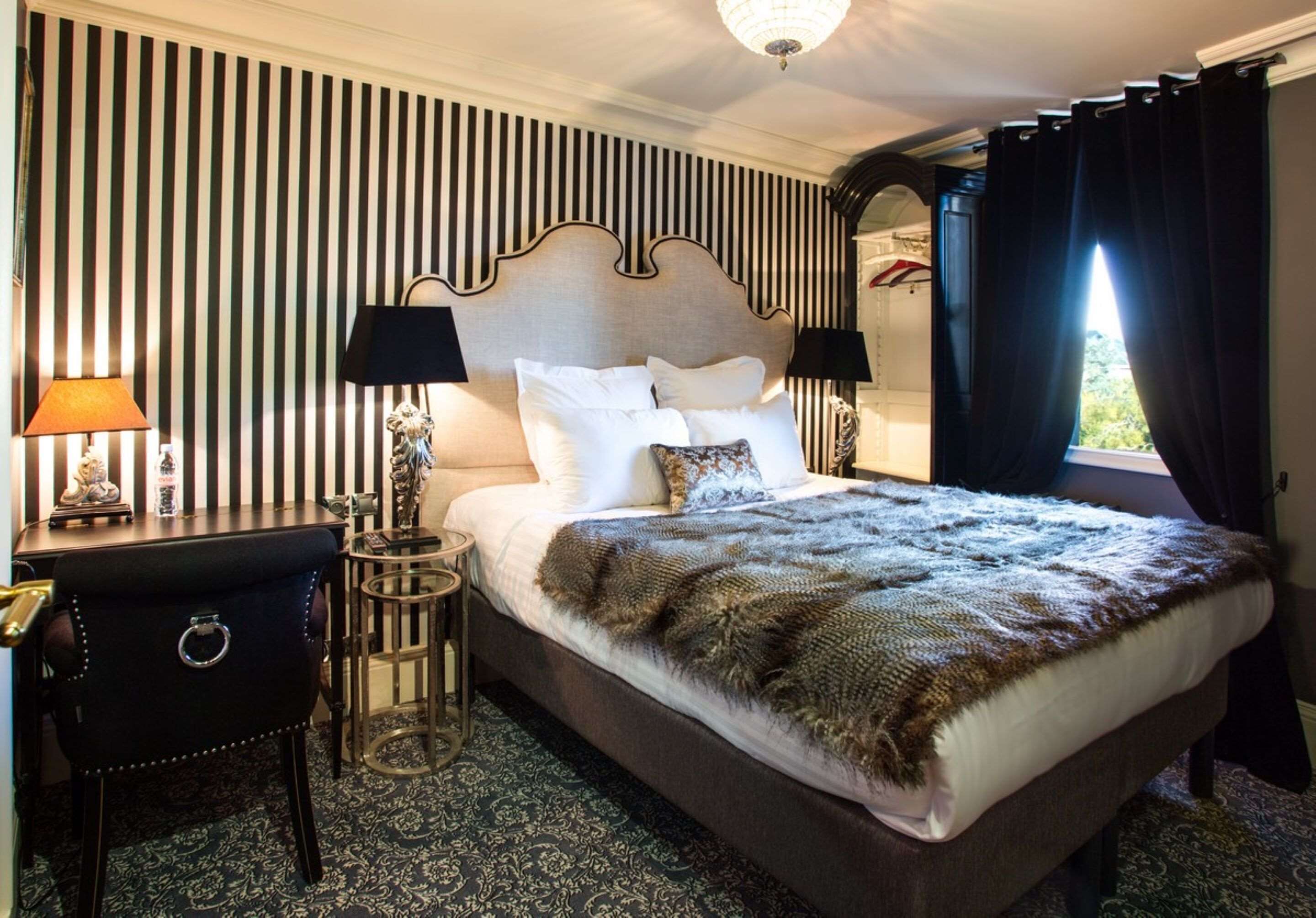 A neatly made bed with a patterned blanket, two bedside lamps, a small table with a lamp, and a dark-colored nightstand.