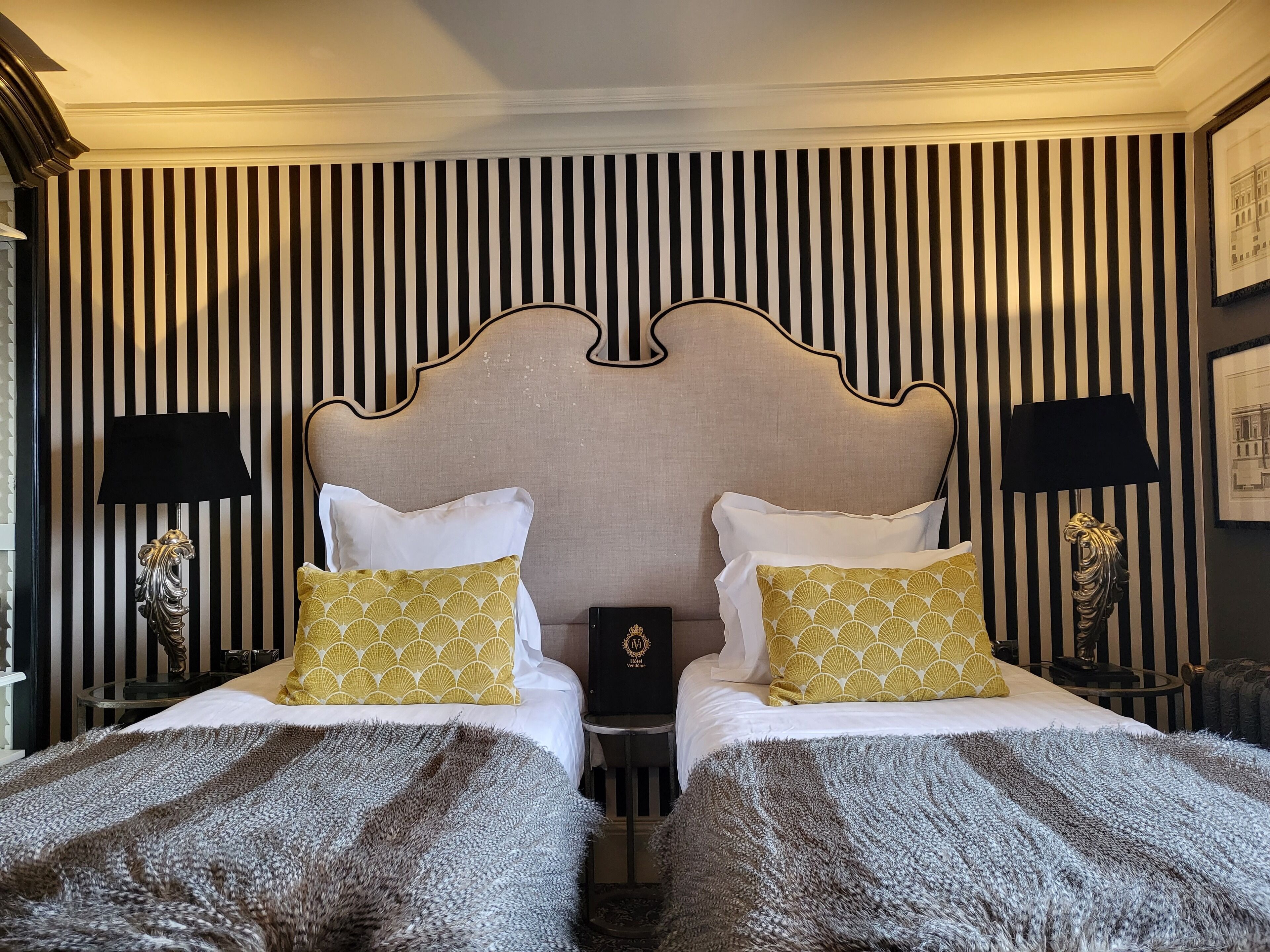 A hotel room with two beds, striped wallpaper, and decorative lamps.