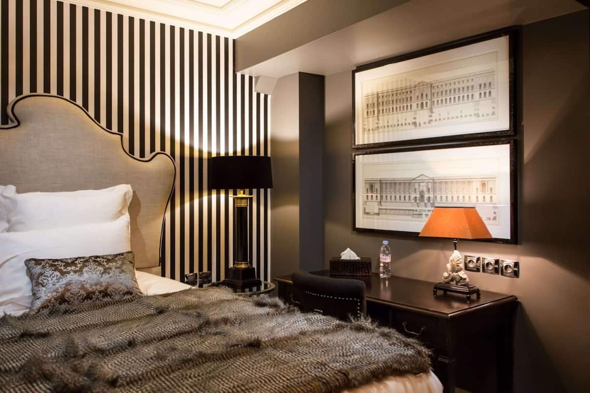 Une chambre d’hôtel avec un lit, un bureau, une lampe et deux dessins d’architecture encadrés accrochés au mur.