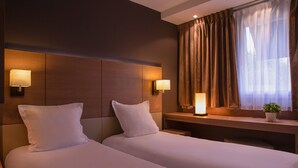 Habitación de hotel con dos camas, un escritorio y una ventana con cortinas.