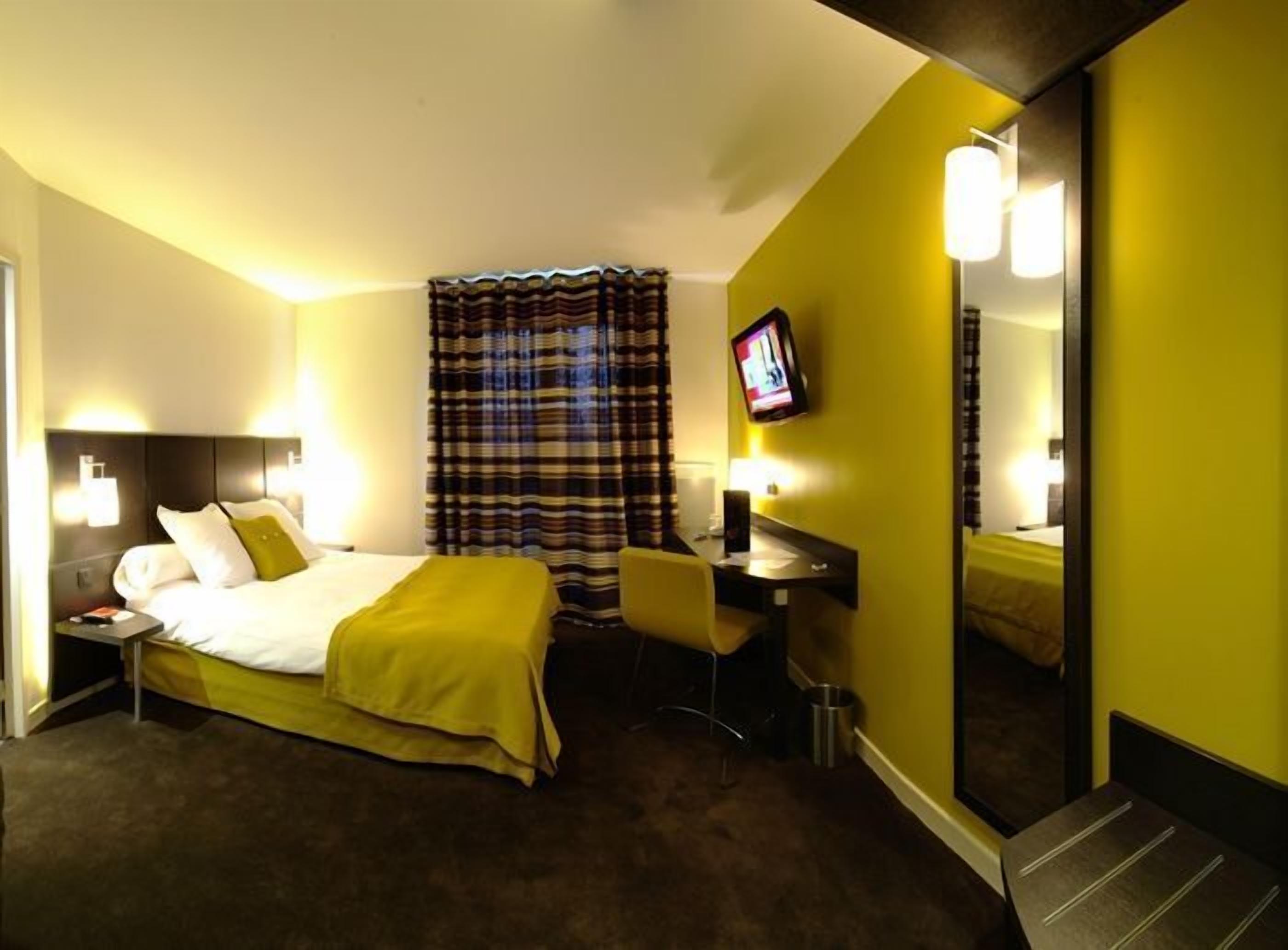 A hotel room with a bed, a desk, a chair, a television, and a mirror.