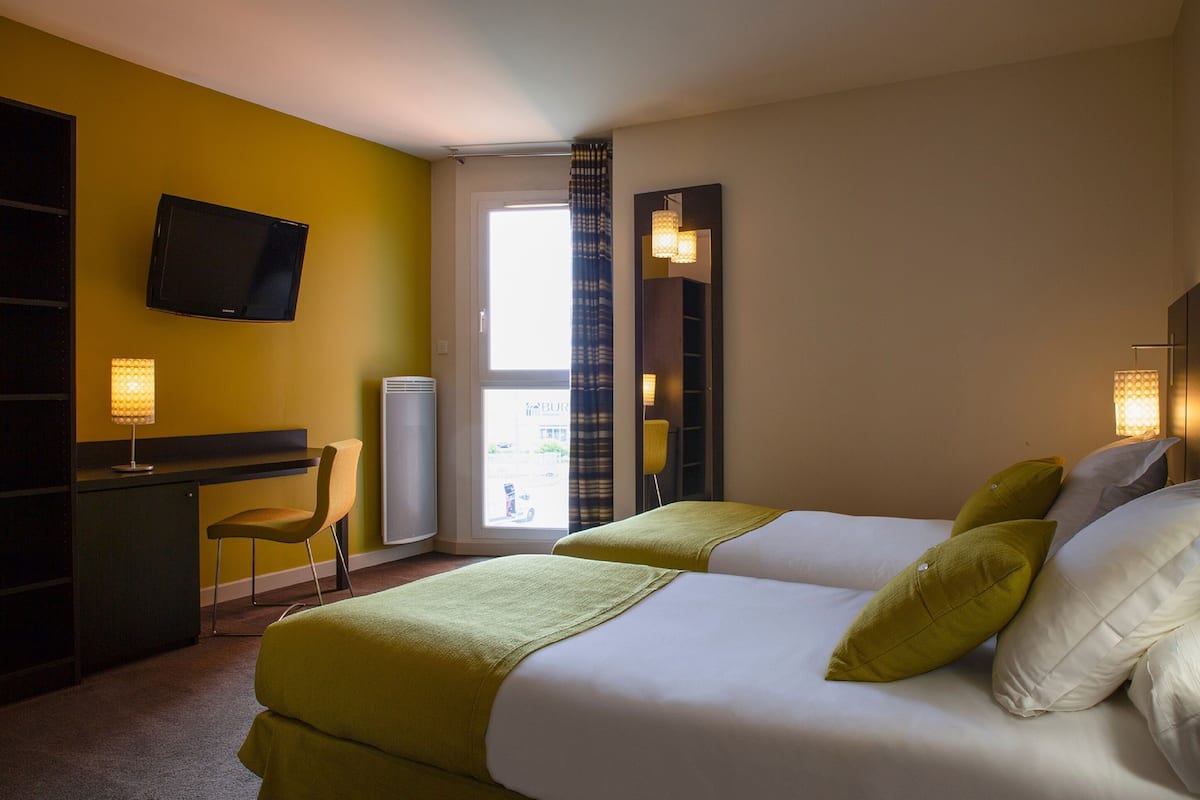 Habitación de hotel con dos camas, un escritorio, una silla, un televisor y una ventana con cortinas.