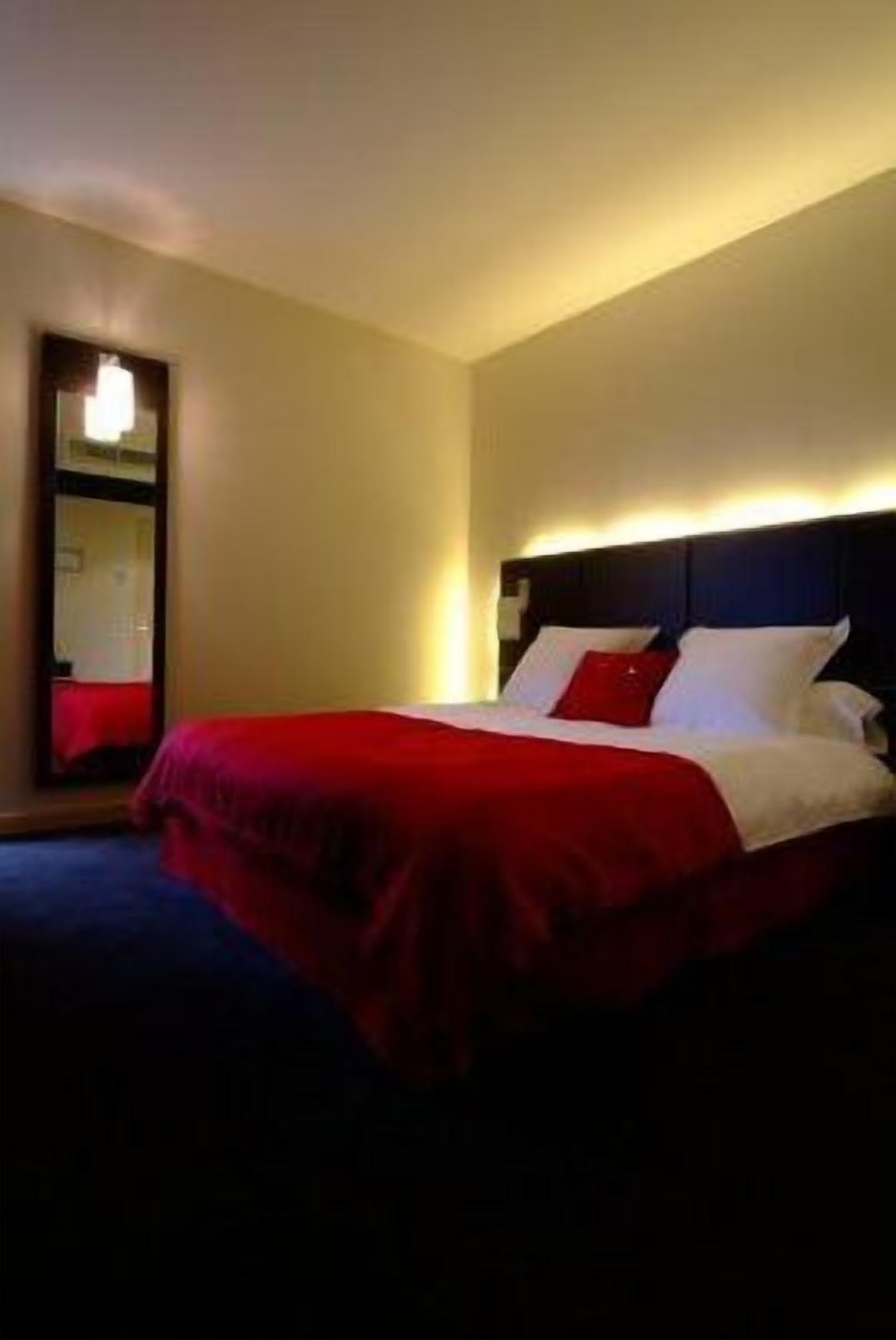 Een hotelkamer met een bed, nachtkastje en spiegel.