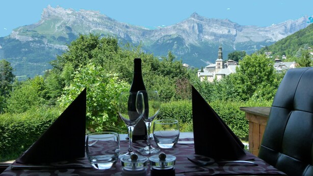 A table set for two with a view of mountains and a church in the background. - Chalet Liberty Mont-blanc (Saint-Gervais-les-Bains)