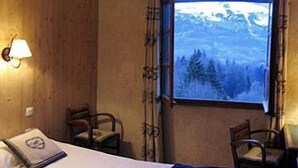 A room with a bed, two chairs, a window with a view of a snowy landscape, and a wall-mounted lamp. - Chalet Liberty Mont-blanc (Saint-Gervais-les-Bains)