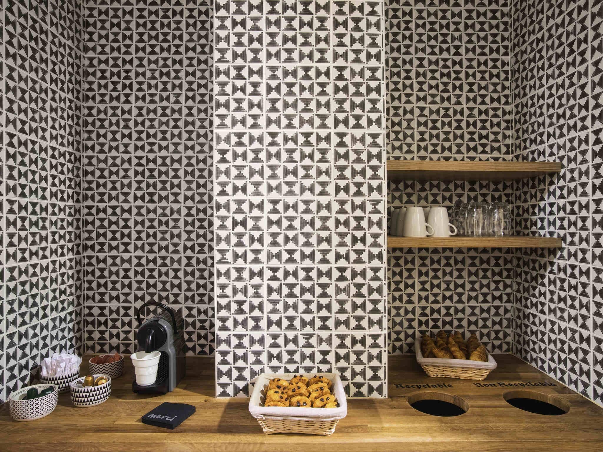 Una habitación con papel tapiz estampado, una mesa de madera con cestas y estantes con vasos y copas.