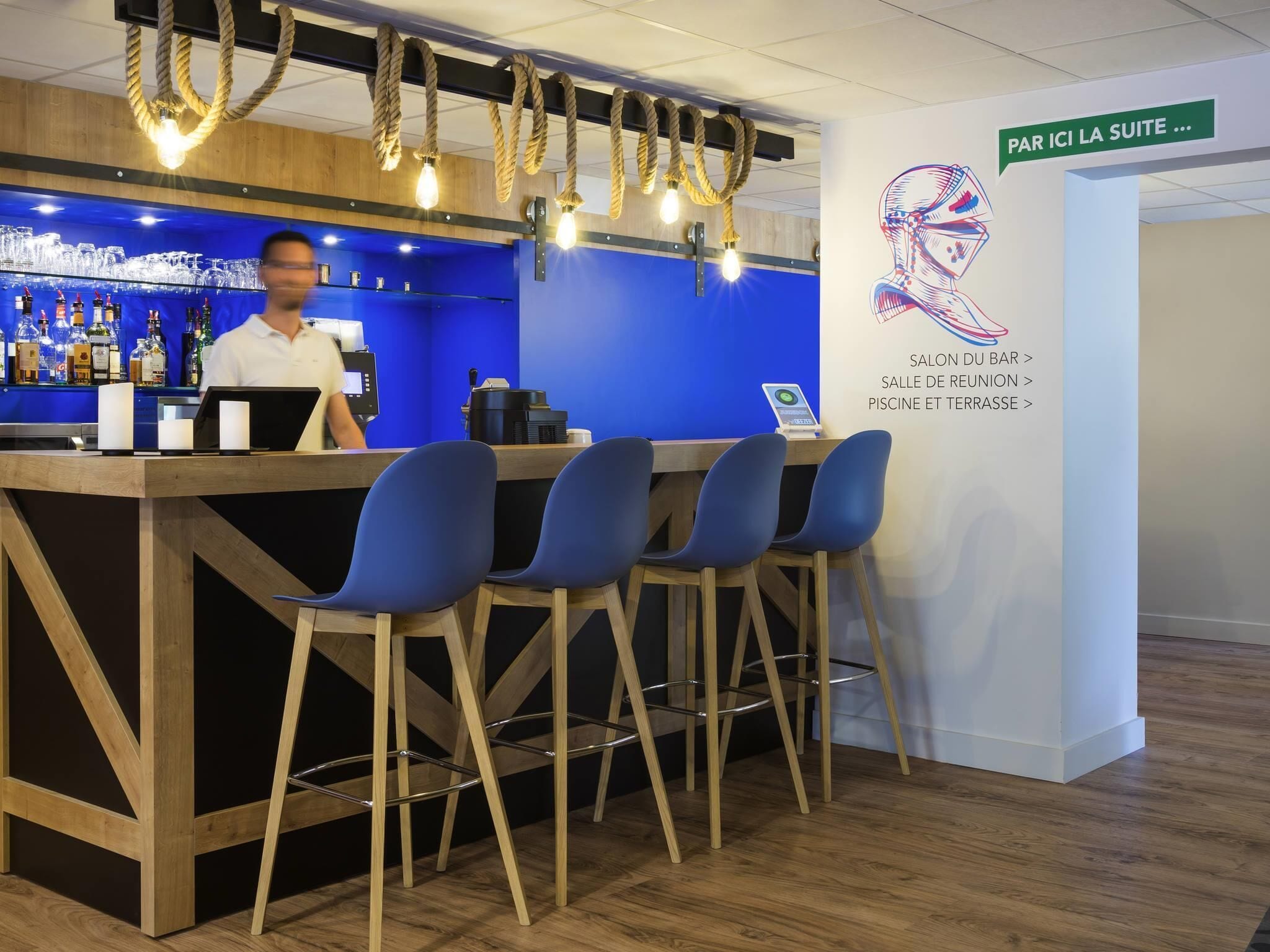 A bar area with a bartender, blue seating, and a sign indicating the suite location.