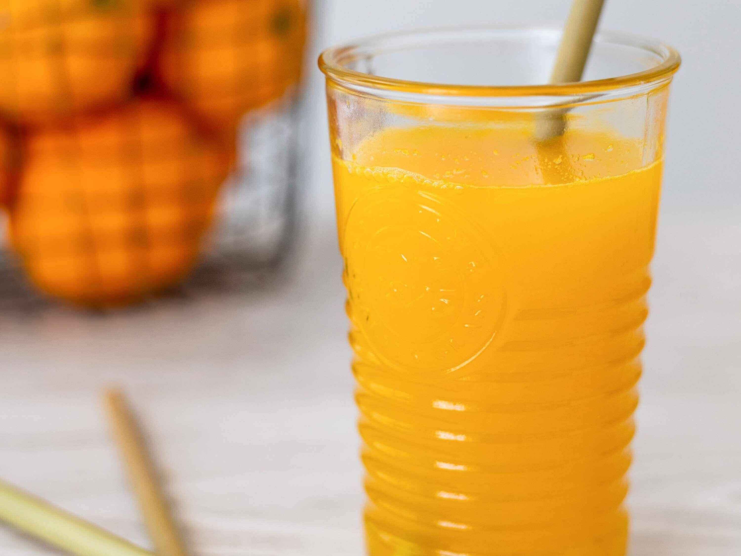 A glass of orange juice with a straw in it.