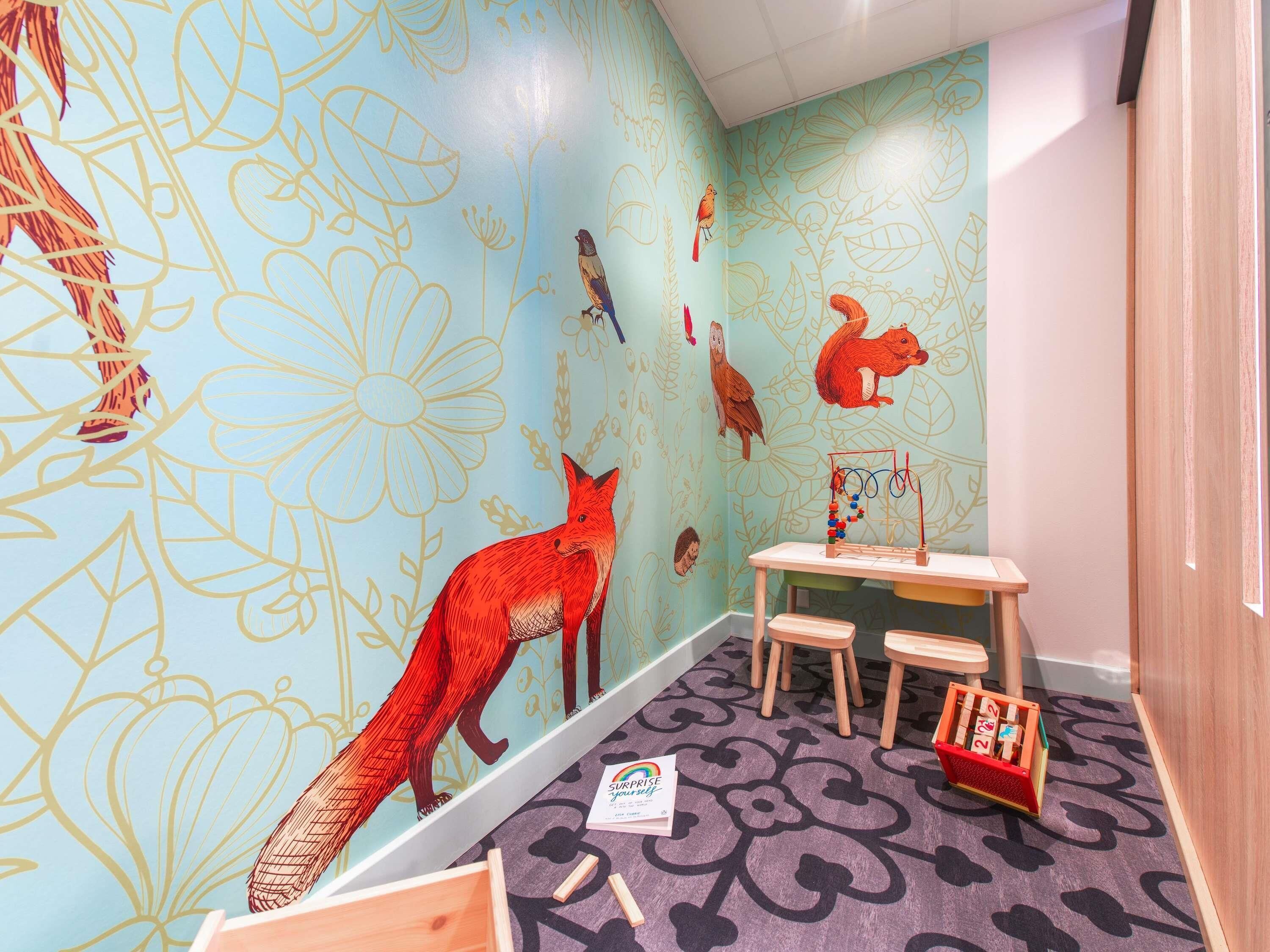 Un cuarto de juegos infantil con un mural de animales, una mesita con sillas y un baúl de juguetes.