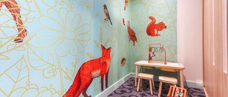 A children's playroom with a mural of animals, a small table with chairs, and a toy chest.