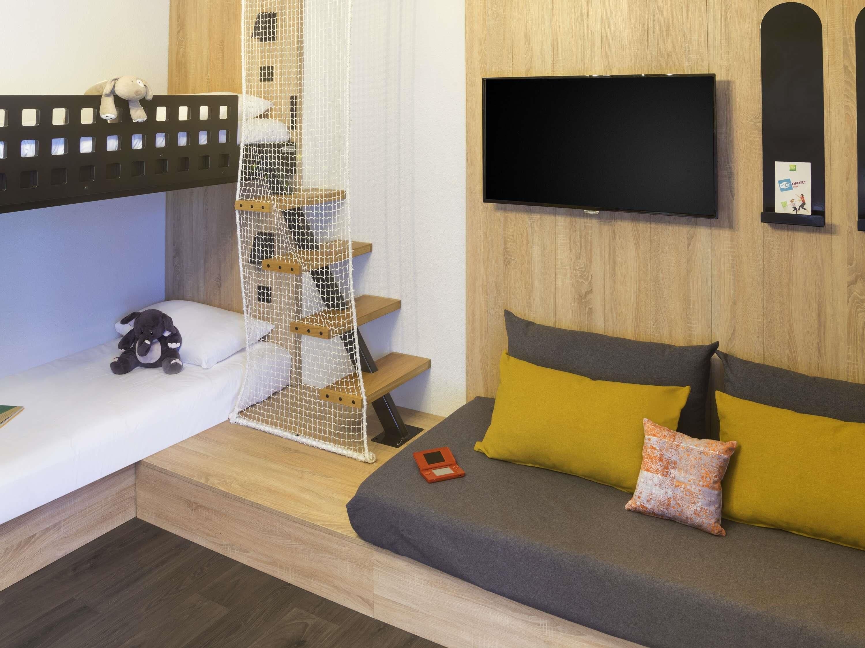 A bedroom with a bed, a sofa, a TV, and a small staircase with a net.