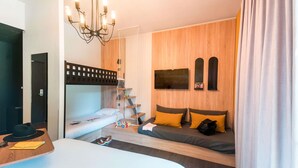 Una habitación de hotel moderna con una cama litera, un escritorio con silla, un candelabro y un televisor montado en la pared.