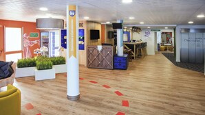 Zona de recepción con mostrador de madera, un letrero azul y blanco, y un área de estar con sillas y una mesa.