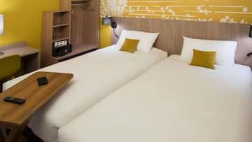 Habitación de hotel con dos camas, una mesita de noche de madera, un escritorio y una pared con motivos decorativos.