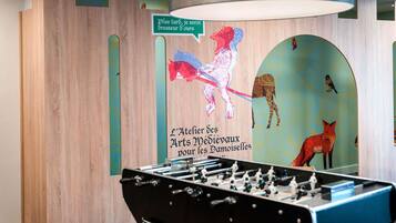 Una habitación con mesa de fútbol, paredes de madera y un mural con animales y texto.