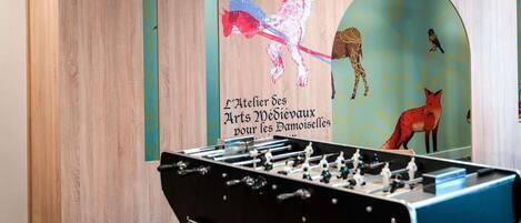 A room with a foosball table, wooden panel walls, and a mural with animals and text.