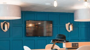 Una habitación moderna con pared azul, televisor montado y mesa de madera con una computadora portátil y un sombrero negro.