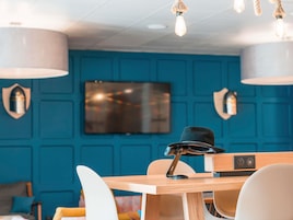 Una habitación moderna con pared azul, televisor montado y mesa de madera con una computadora portátil y un sombrero negro.