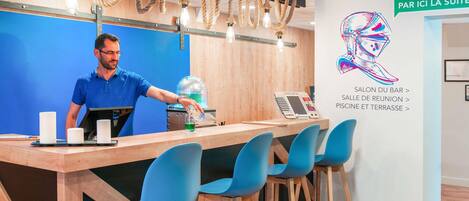 A reception desk with a man standing behind it, a bar area with blue chairs, and a wall with directional signs.
