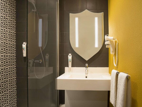 Un baño con cabina de ducha de vidrio, un lavabo blanco y un espejo con diseño tipo escudo.