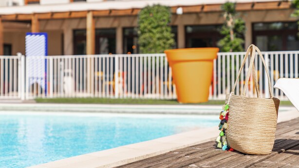 Zona de piscina con una cesta de mimbre y una silla blanca.