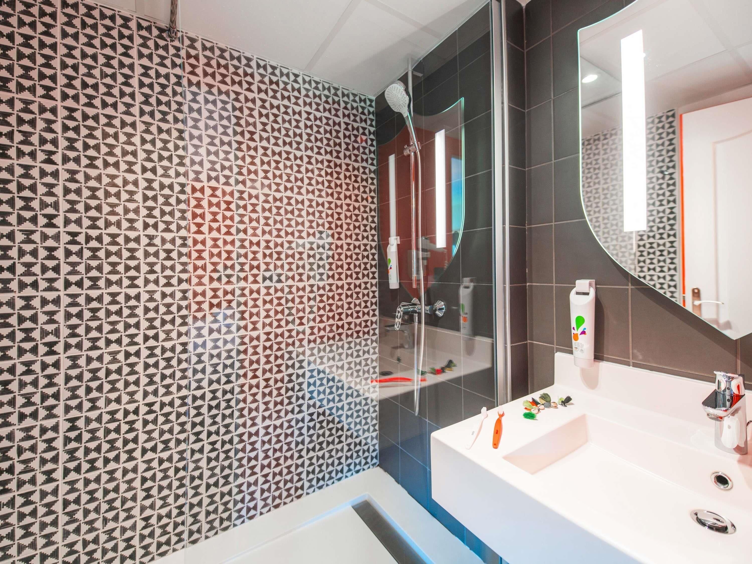 Een moderne badkamer met een wand met een geometrisch patroon, een glazen douchecabine en een wit wastafelmeubel met spiegel.