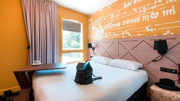 Una camera d'albergo con un letto, una scrivania, una sedia, una valigia e un tavolino.
