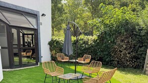 A patio with four wicker chairs and a table, surrounded by a hedge and a white building with a glass door. - ibis Styles Paris Saint Denis Plaine (Saint-Denis)