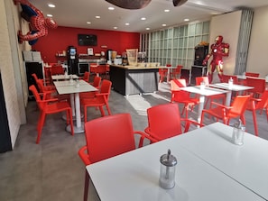 A restaurant with red chairs and tables, a counter, and a Spider-Man decoration.