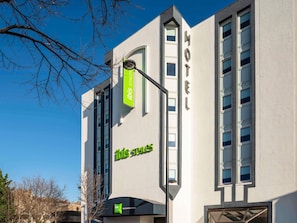 Een modern hotelgebouw met een goed zichtbaar 'ibis style' bord, veel ramen en een heldere lucht.