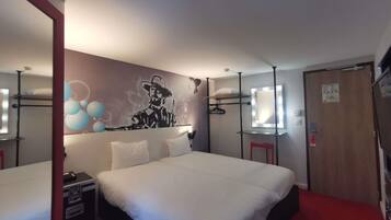 Een hotelkamer met een groot bed, een spiegel met verlichting, een rode stoel en een muur met een afbeelding.