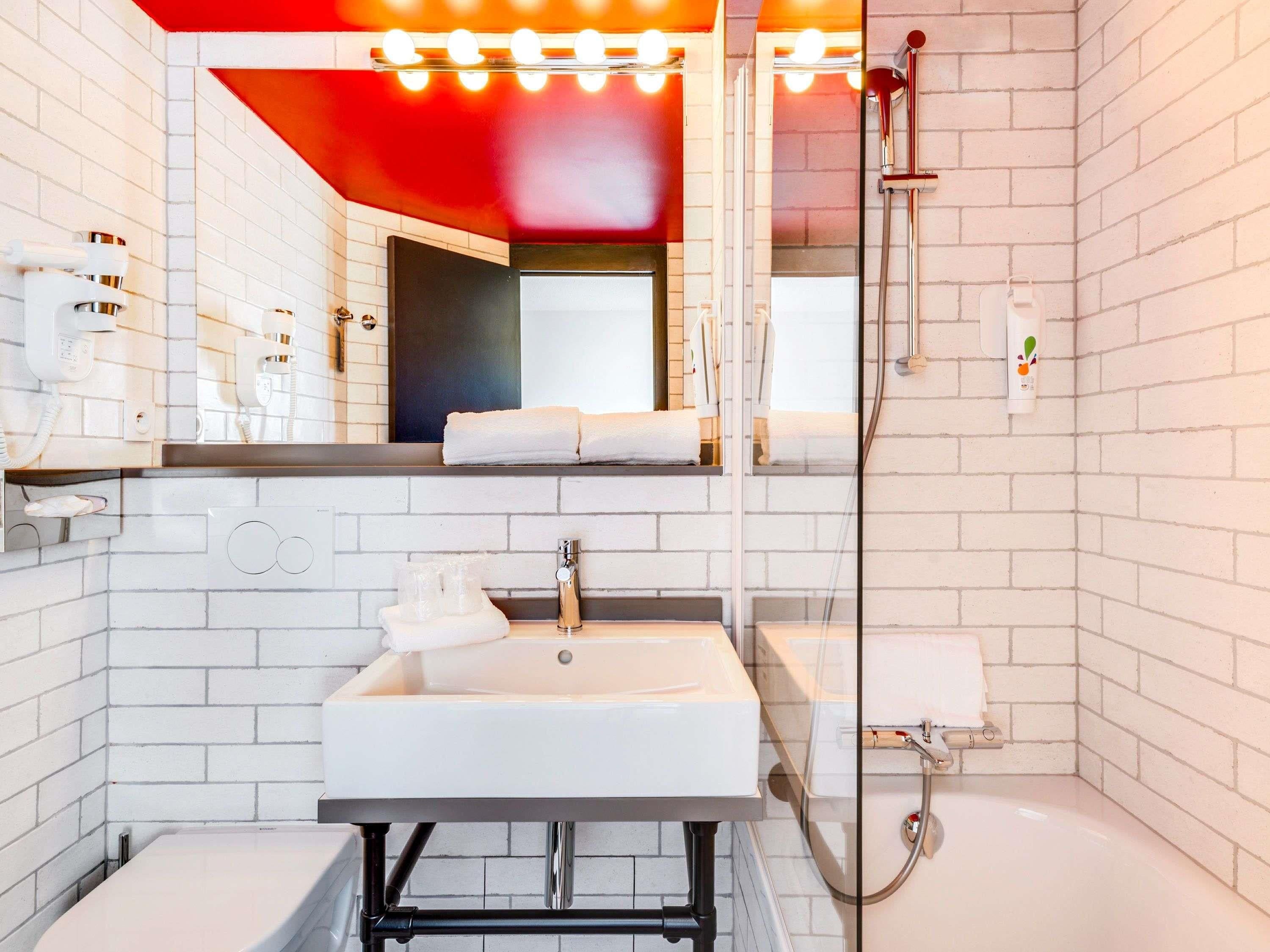 A modern bathroom with white subway tiles, a white sink, a mirror with lights, a shower, and a towel rack.