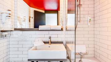 A modern bathroom with white subway tiles, a white sink, a mirror with lights, a shower, and a towel rack.