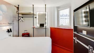 Ein Hotelzimmer mit Bett, roter Akzentwand, großem Spiegel, Fenster mit Blick auf die Stadt und Fernseher.