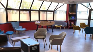 A room with a foosball table, multiple chairs, a bench, and a television.