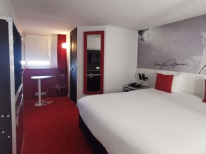 A hotel room with a bed, a desk, a chair, a mirror, a nightstand, and a wall with a signature. - ibis Styles Paris Saint Denis Plaine (Saint-Denis)